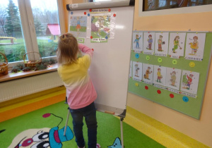 Dziewczynka przywiesza na tablicy ilustracje prezentującą jedno z praw dziecka.